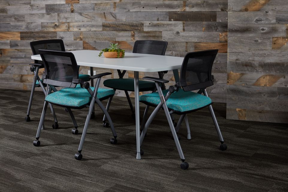 Compact meeting area with a rectangular table and four mesh-backed chairs with teal seats, set against a rustic wood-paneled wall.